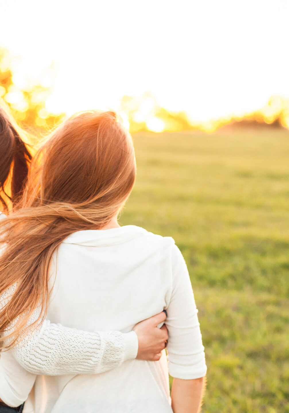 Young women in white sweaters are walking on the green field. Best friends